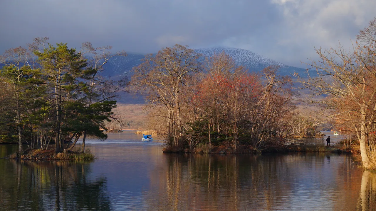 A still lake with bare autumn trees on small islands and hills behind