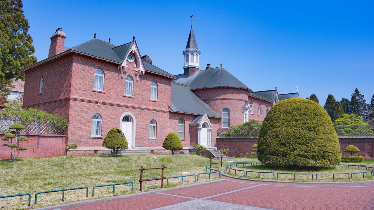 A red brick convent building with a spire, behind a clipped garden