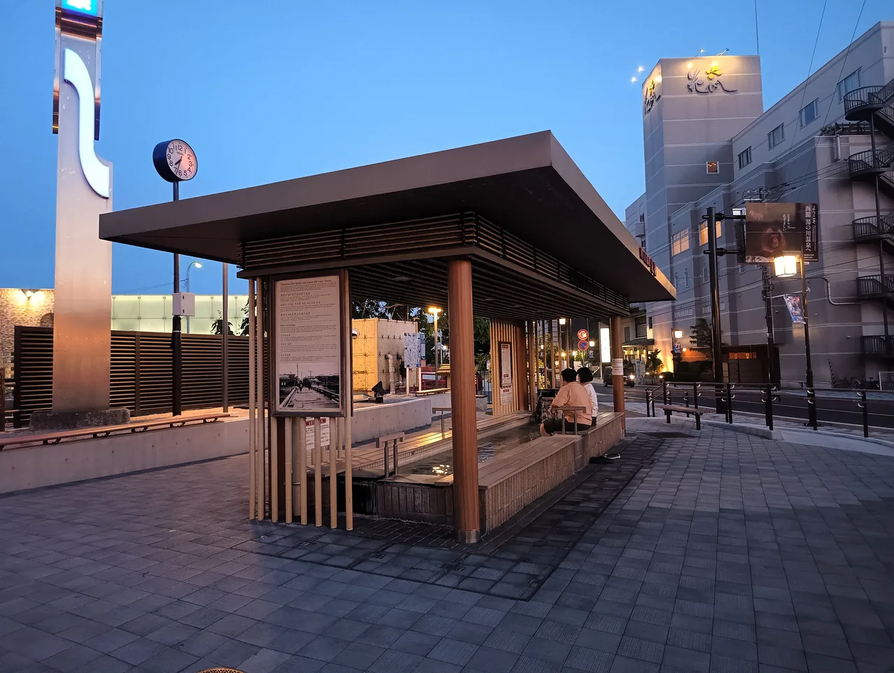 A covered wooden foot bath pavilion on a street at dusk