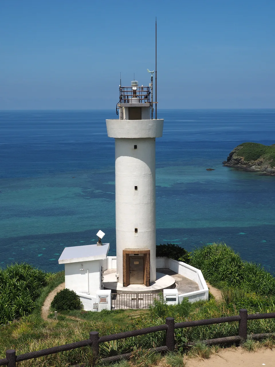 A white lighthouse on a green headland above the sea