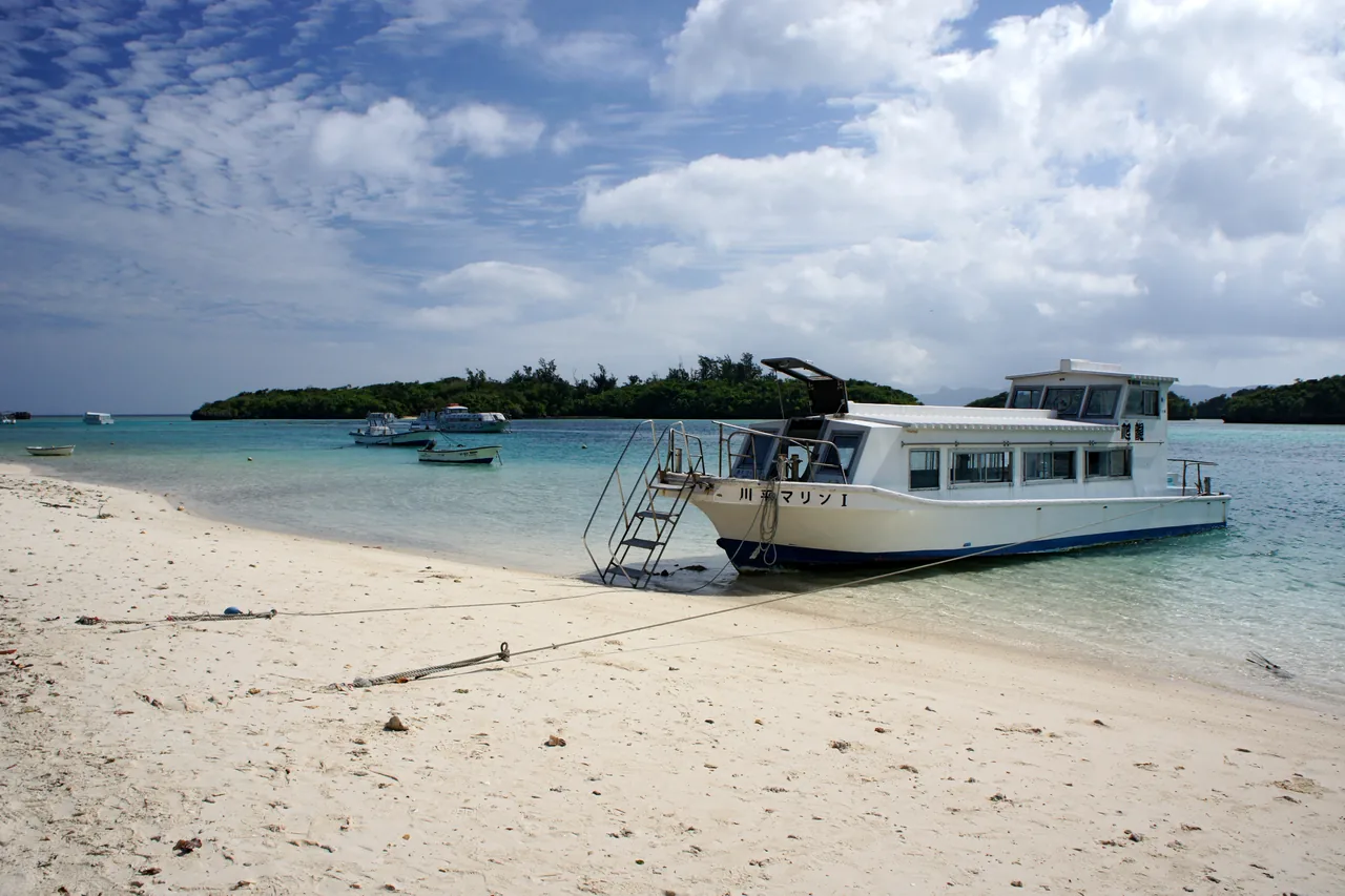 A boat on the pale green water of Kabira Bay with wooded islets behind it