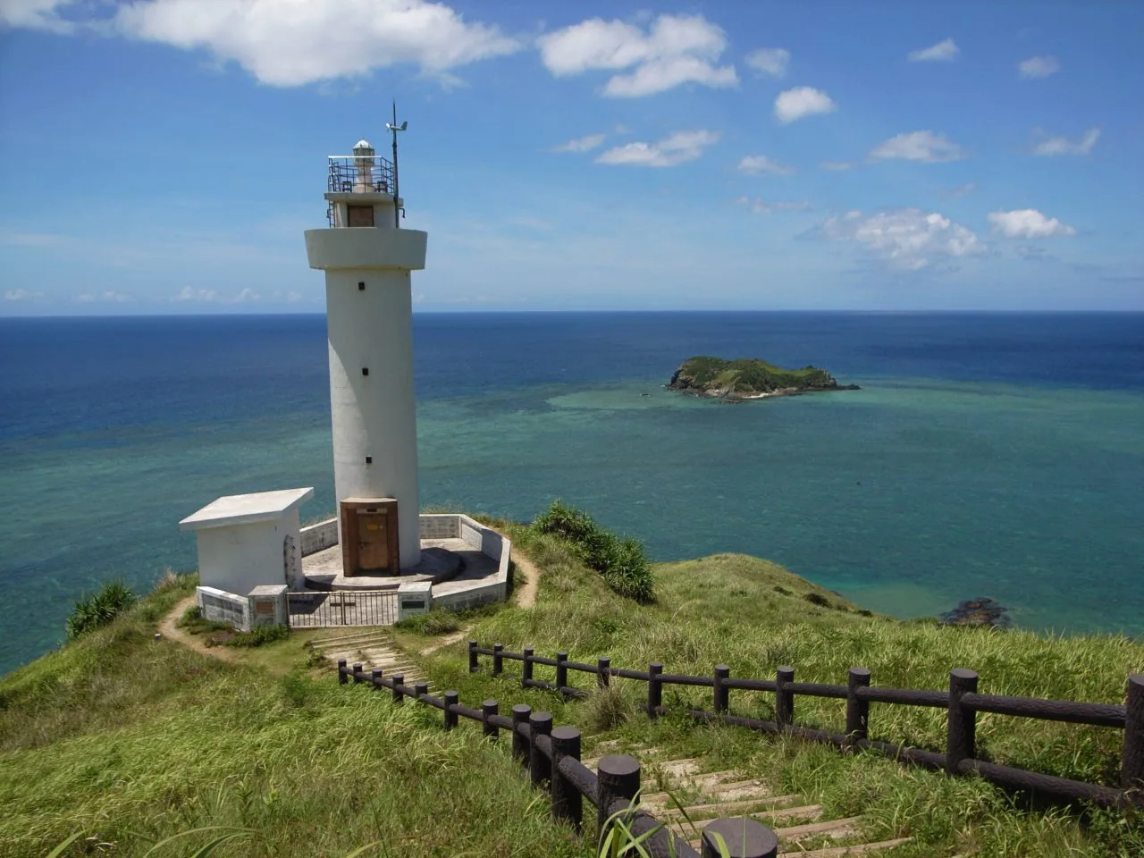 A white lighthouse on a grassy headland with a small island offshore