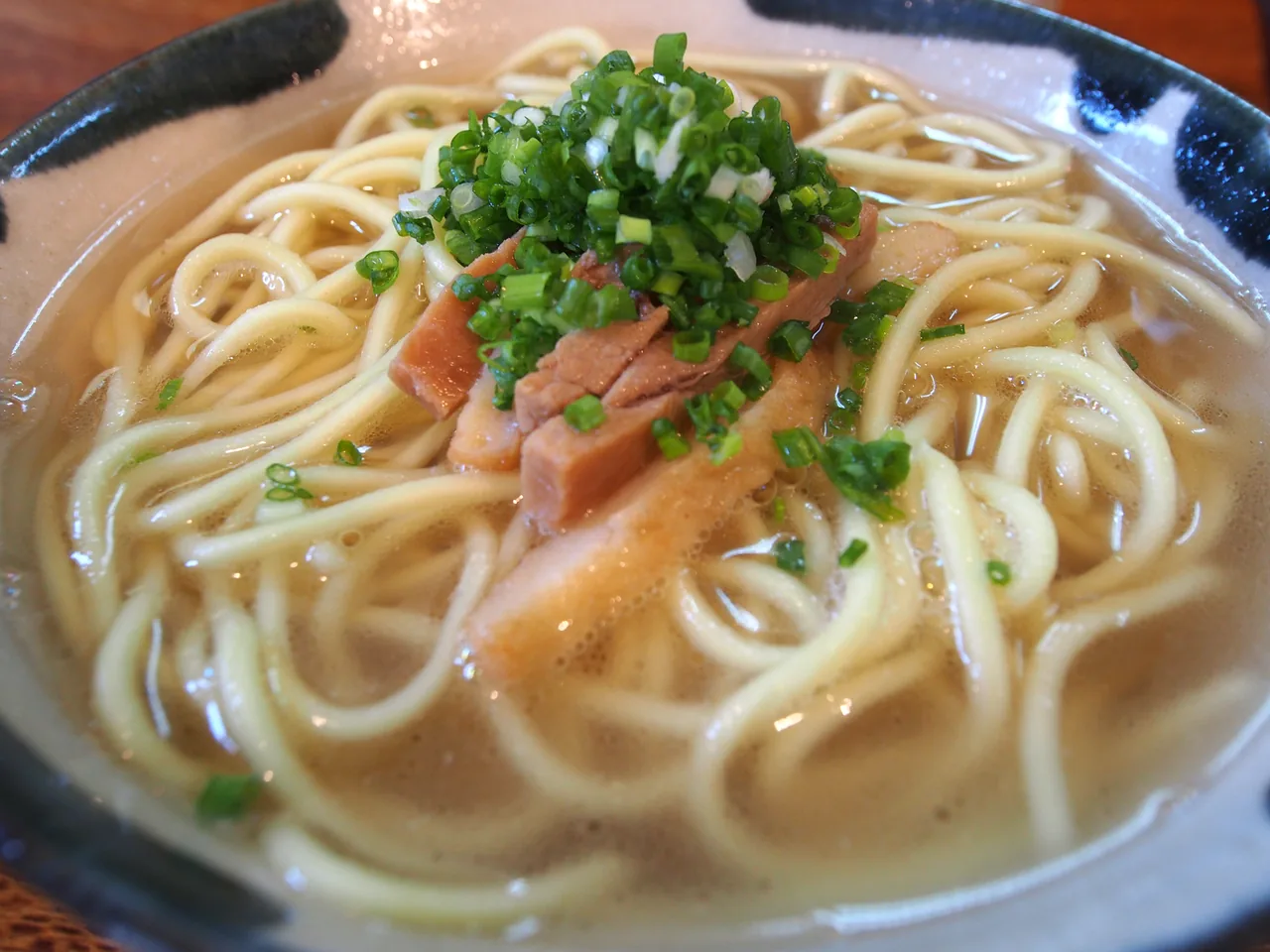 A bowl of Yaeyama soba with sliced meat and spring onion in a clear broth