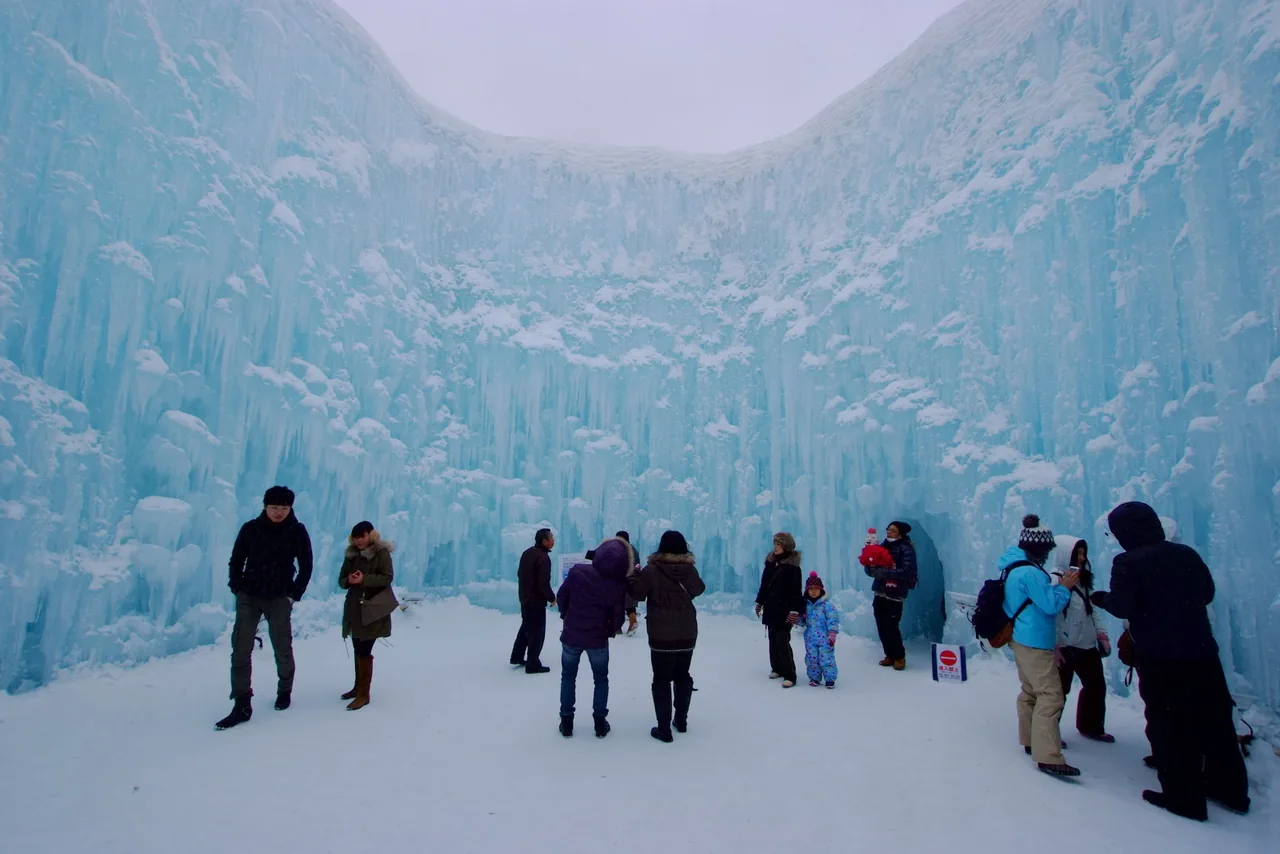 People walking between blue ice pillars and ice walls in daylight