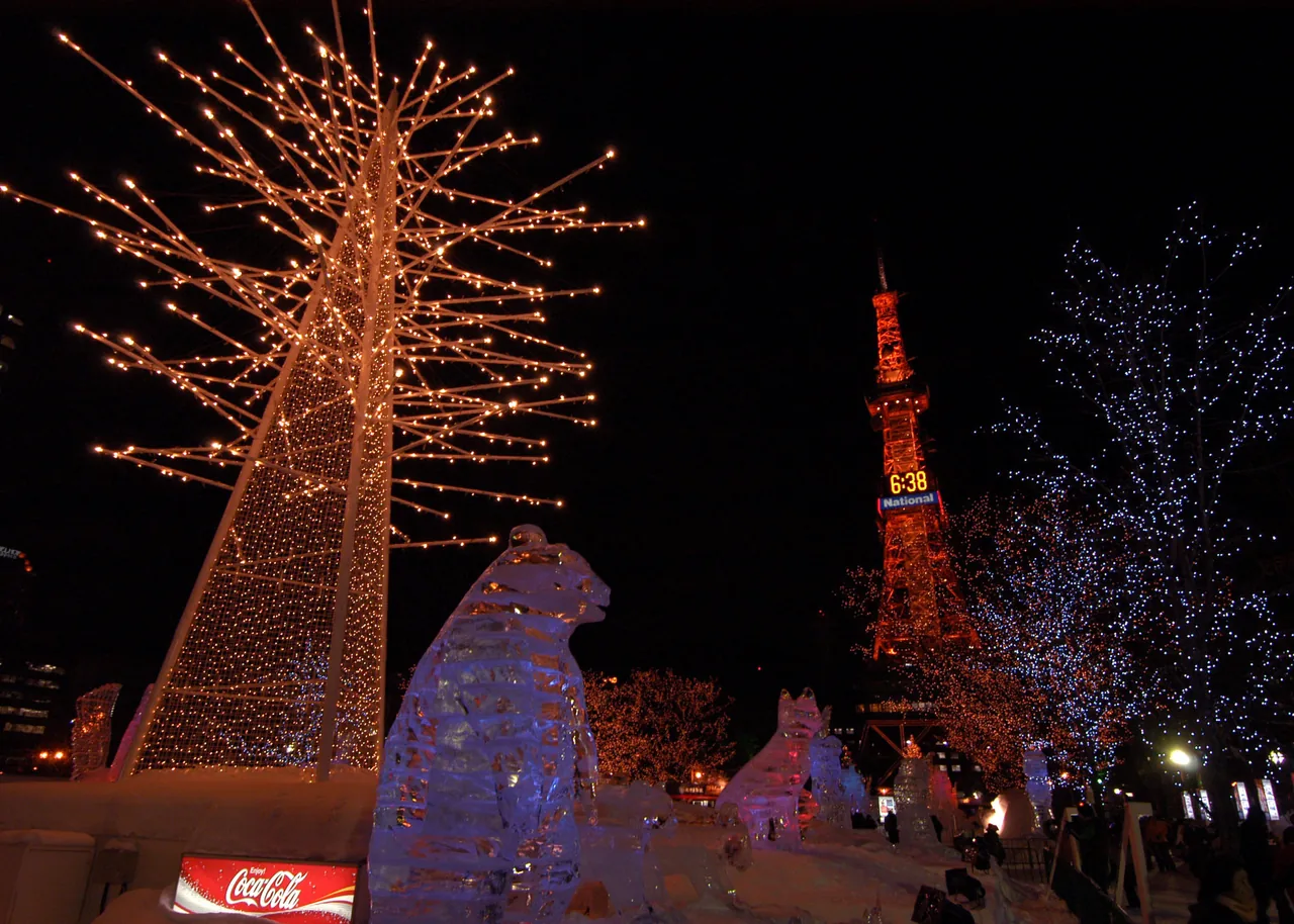 Lit-up trees and ice sculptures at night, with the Sapporo TV Tower beyond