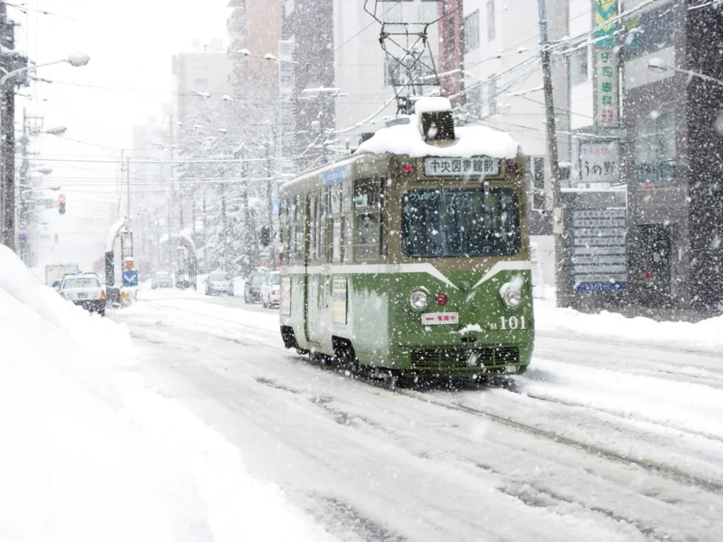 A green streetcar running through heavy snowfall on a Sapporo street
