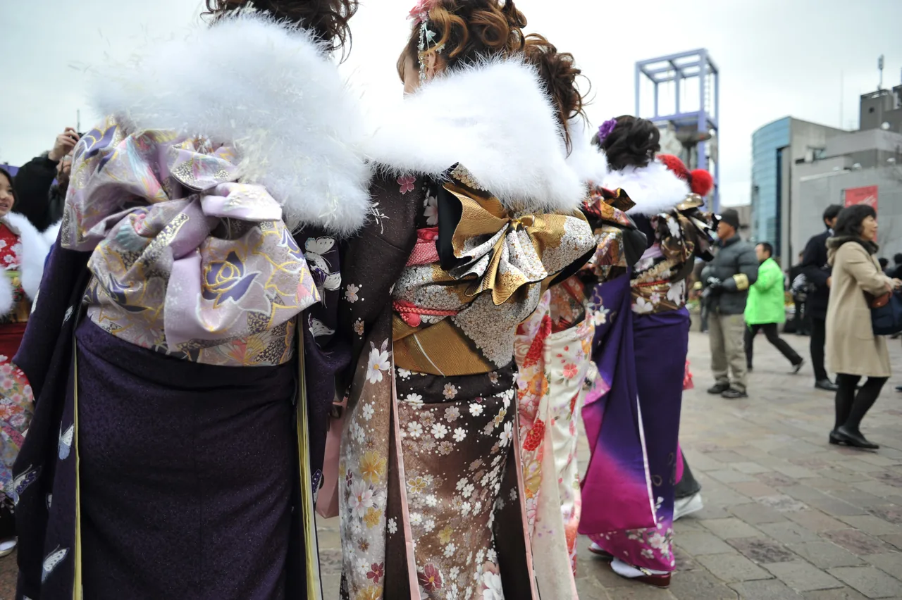 Young women in furisode kimono with white fur stoles and large obi bows, seen from behind