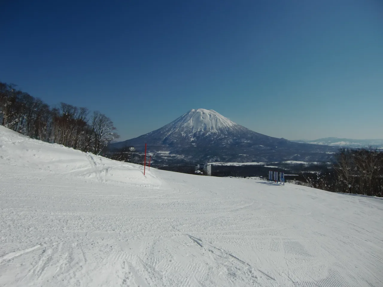 A groomed Niseko ski run with snow-capped Mount Yotei under a blue sky