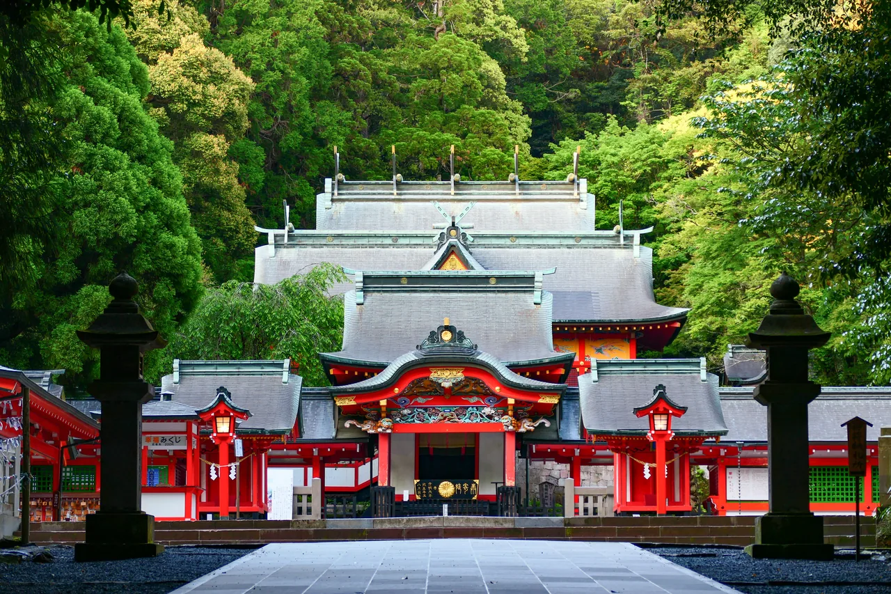The vermilion and white halls of Kirishima Shrine with ornate roof brackets, surrounded by trees