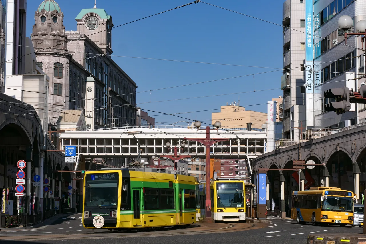 Two Kagoshima city trams waiting at a stop in front of a brick building