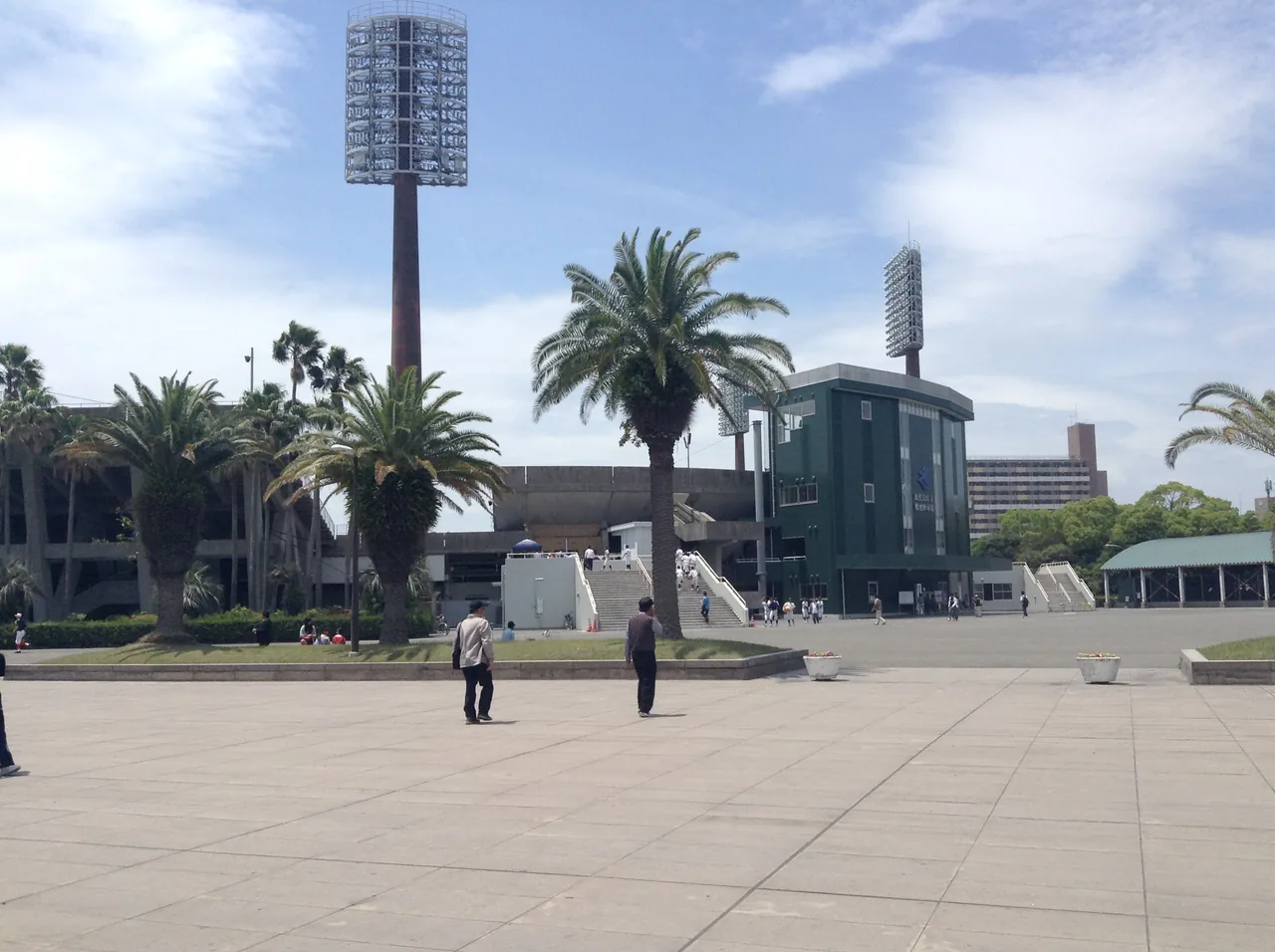 A wide open plaza on the Kamoike waterfront in Kagoshima, lined with palm trees and a floodlight tower