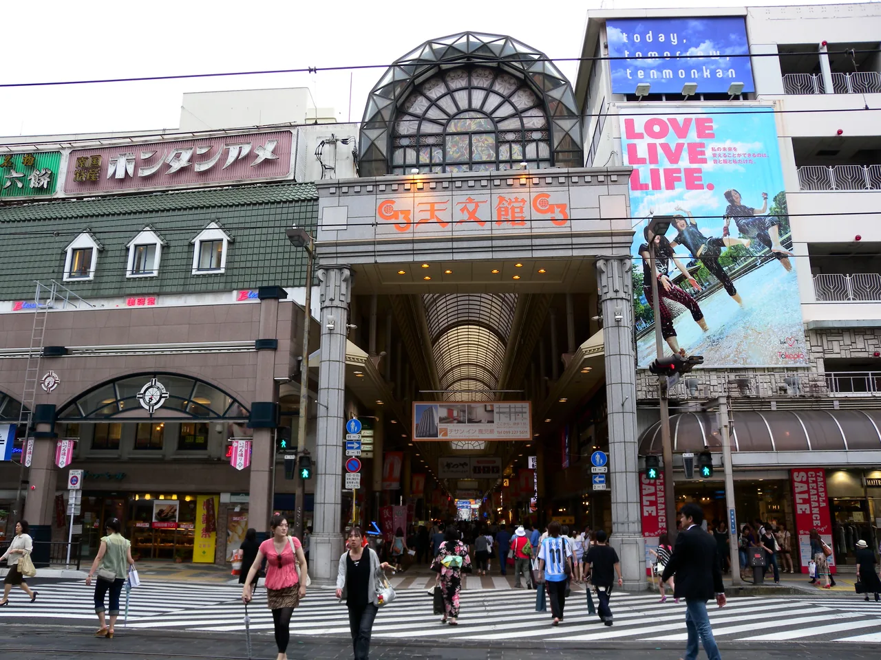 The arched entrance to the Tenmonkan covered arcade in Kagoshima, with people crossing the street in front of it