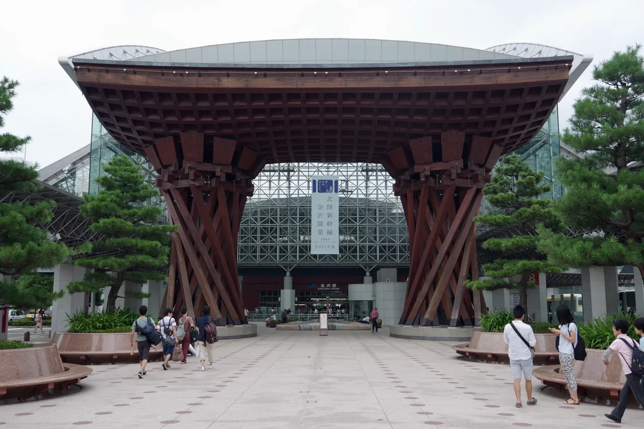 The Tsuzumi gate at the east exit of Kanazawa Station, two large wooden columns supporting a curved roof, with the glass dome of the concourse behind it
