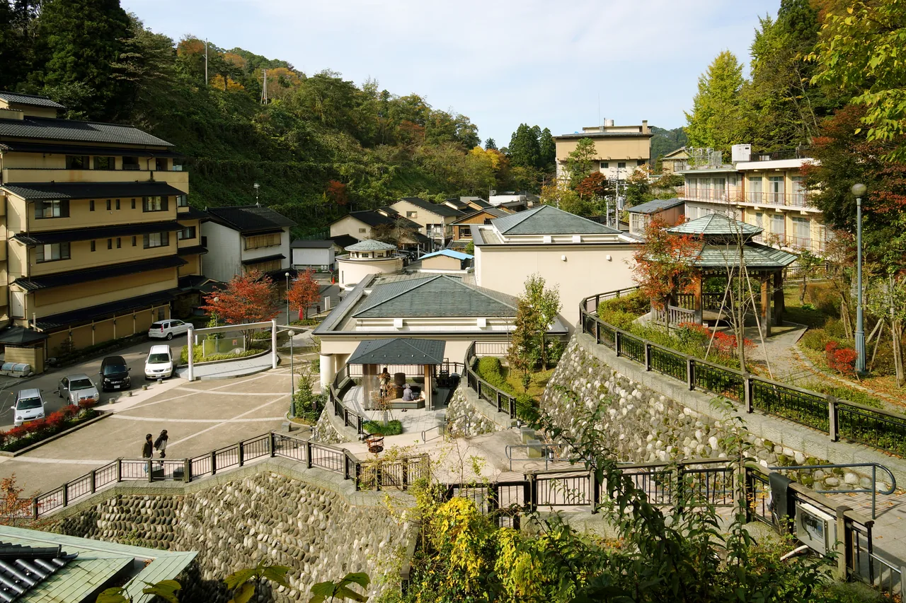 Yuwaku Onsen seen from above, inn buildings lined along a narrow valley with wooded hills rising behind them