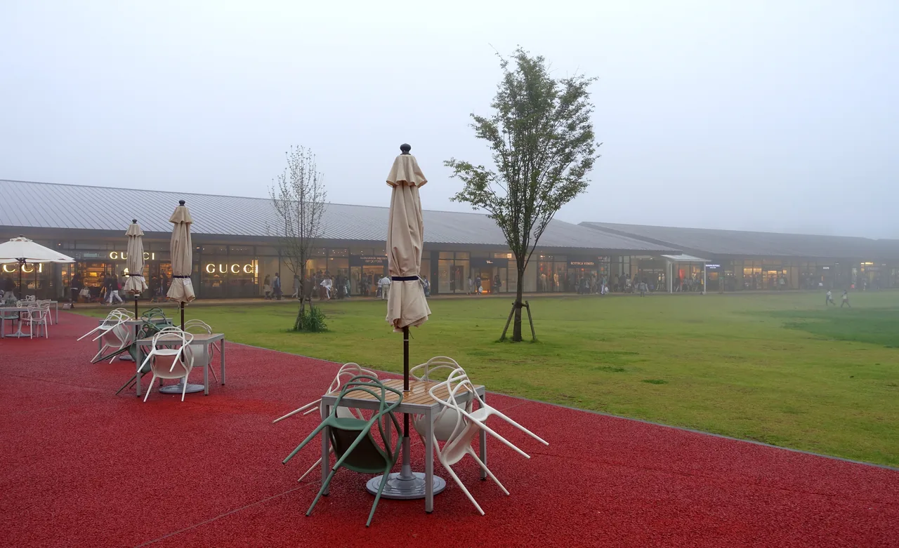A wide lawn with a sculpture on it, ringed by low shop buildings