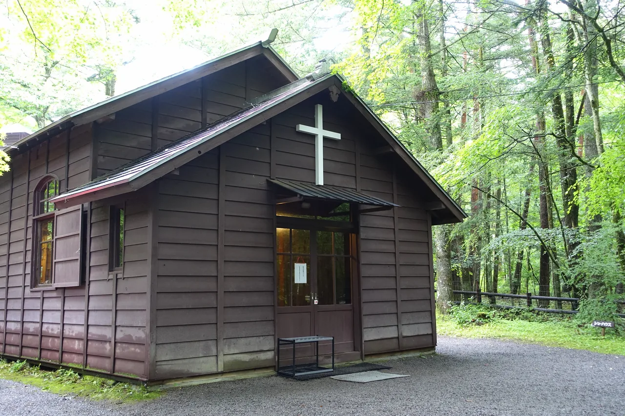 A dark timber chapel with a cross, standing among tall trees