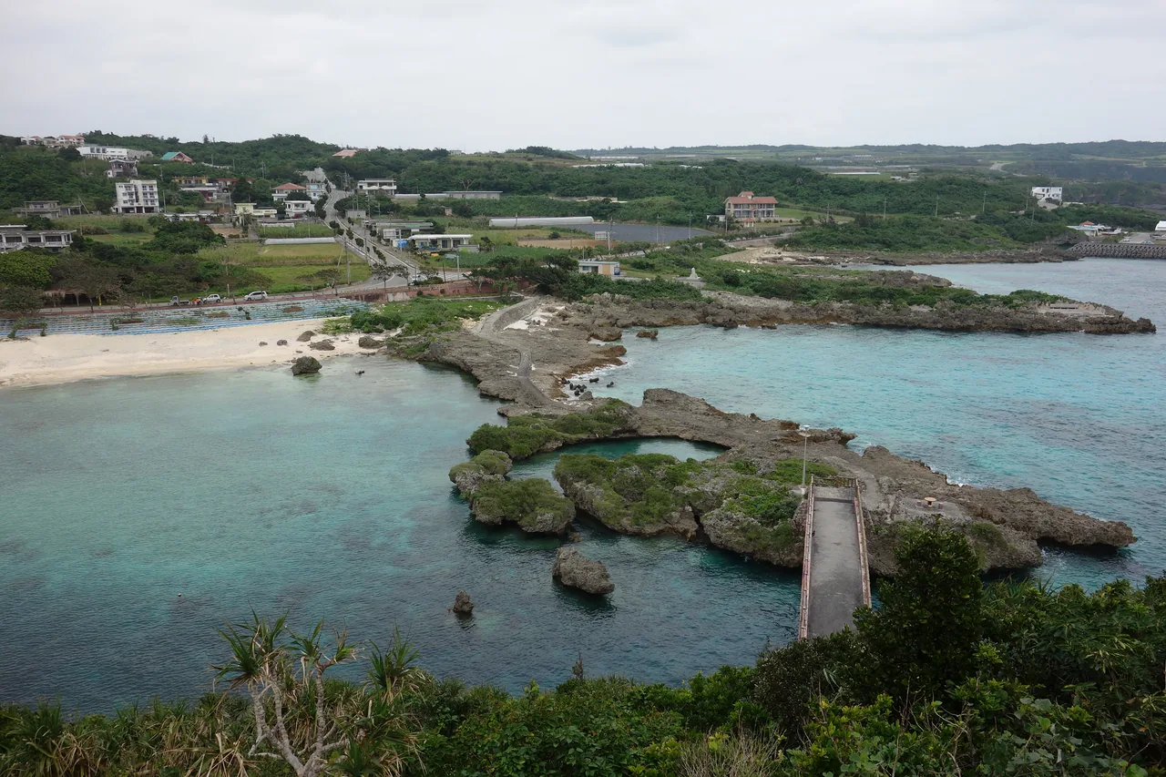 The sheltered inlet of Imgya Marine Garden in Gusukube, with a footbridge crossing the shallow water