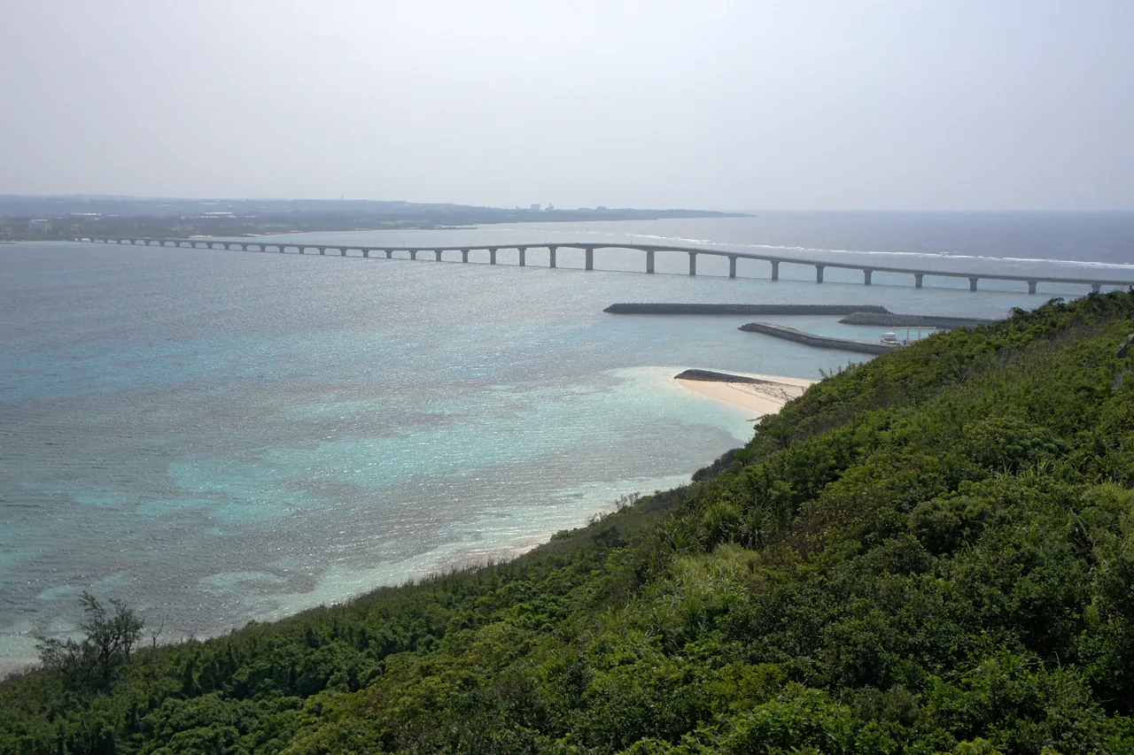 The Kurima Bridge seen from a green slope above it, running low across the water to Kurima island