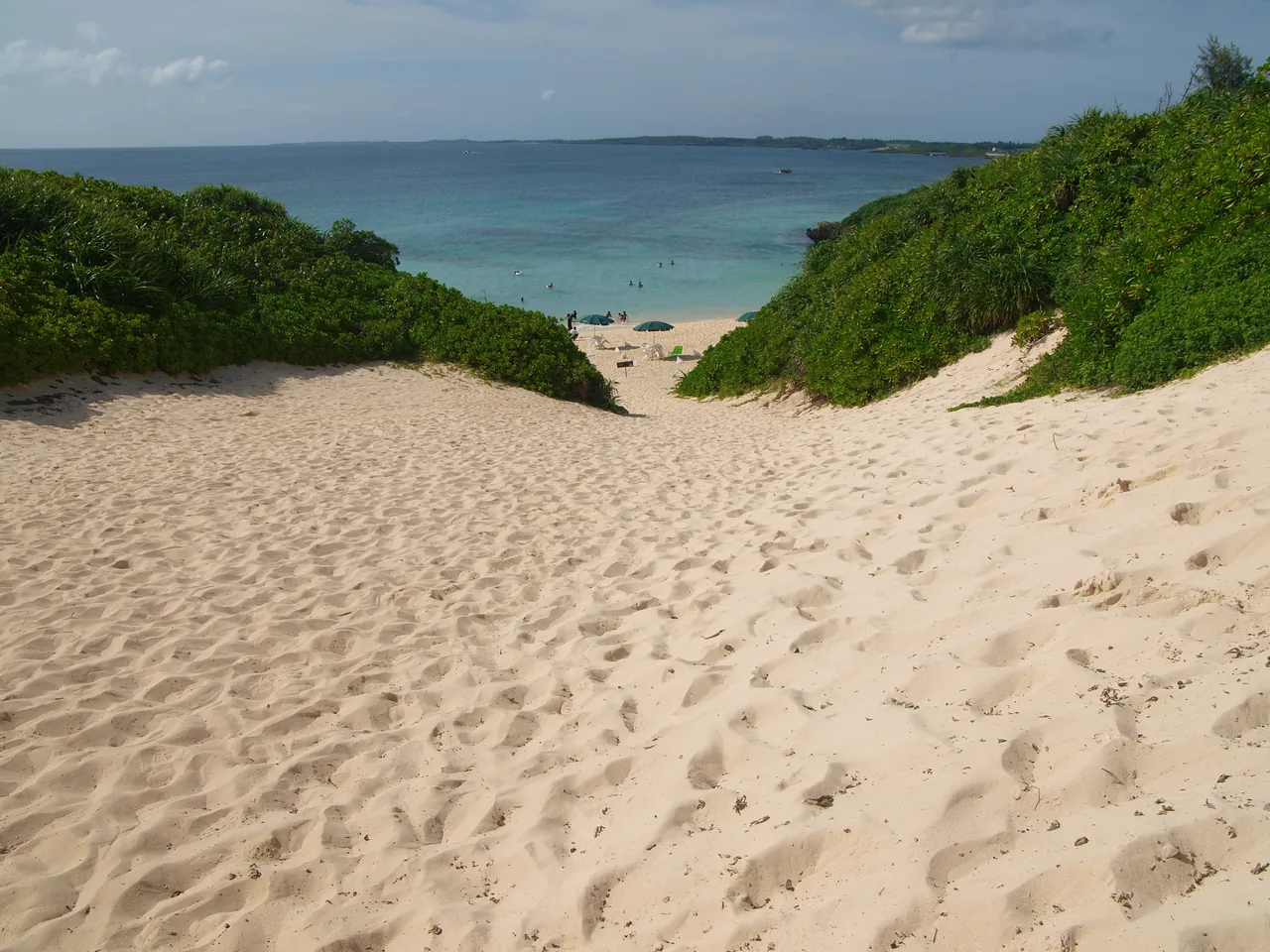 A sand dune dropping away to a beach on the north of Miyakojima, with low green scrub on either side