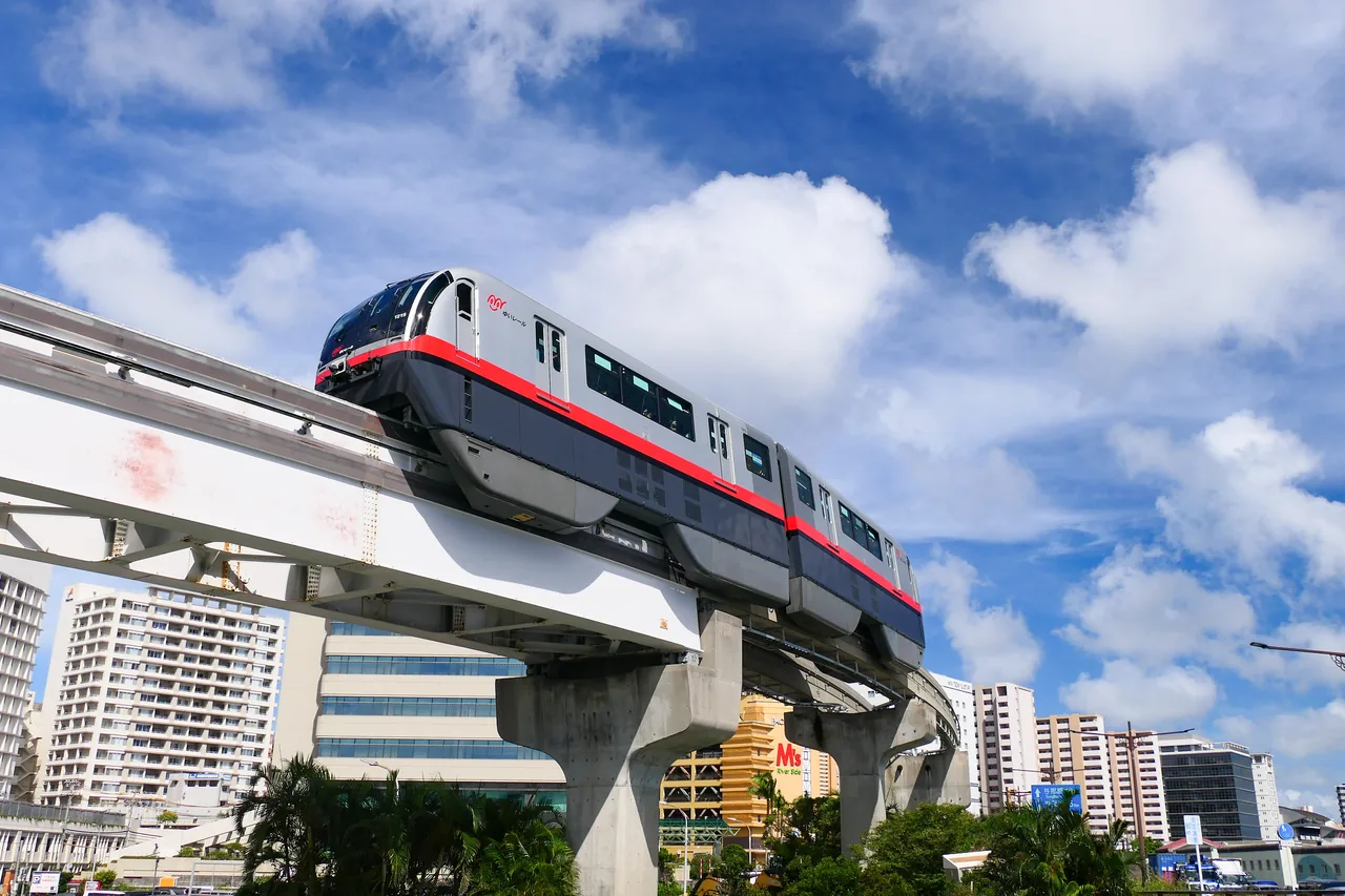 A white two-car monorail train running on an elevated track above the streets of Naha