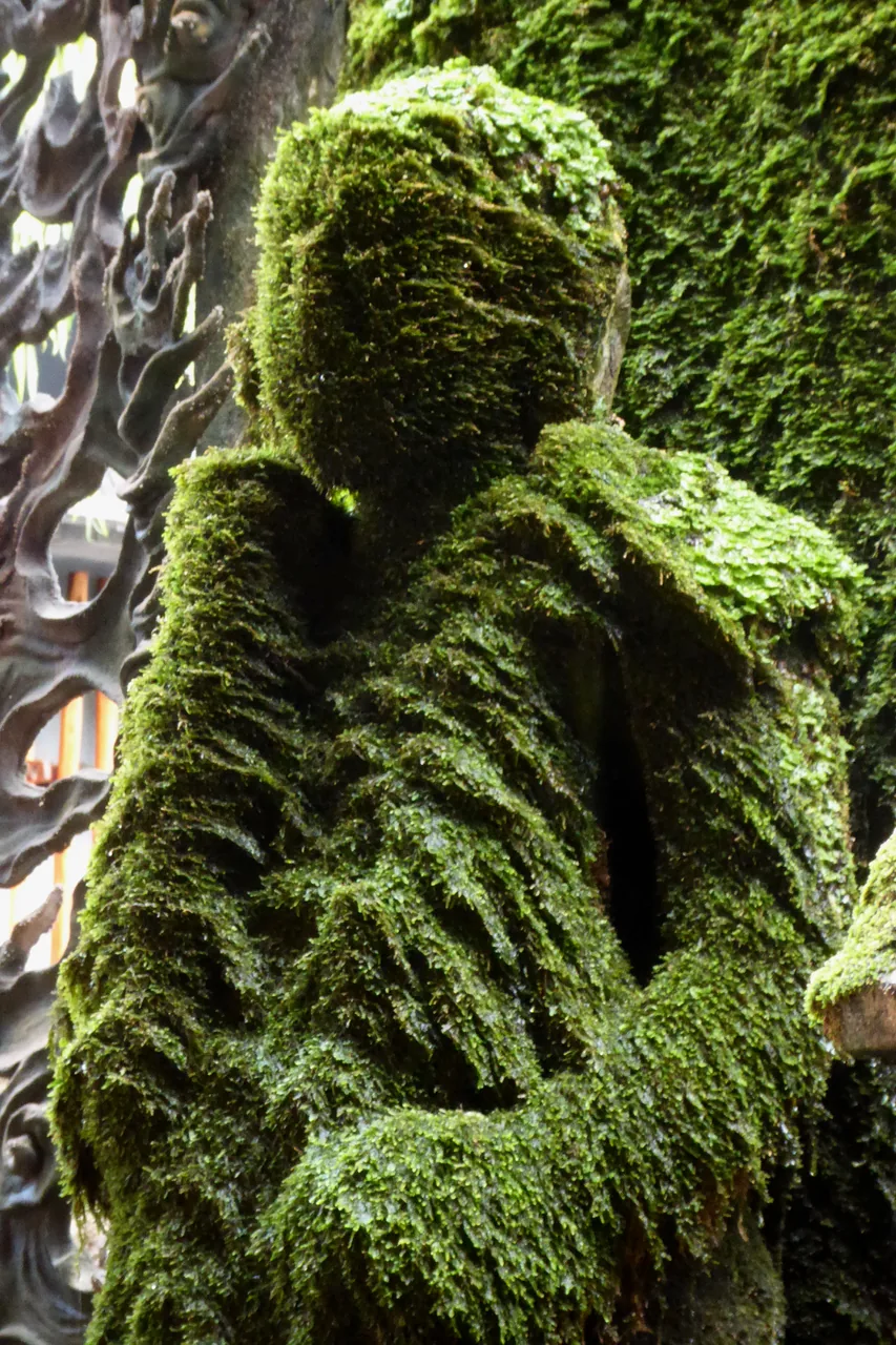 A stone statue covered completely in thick green moss