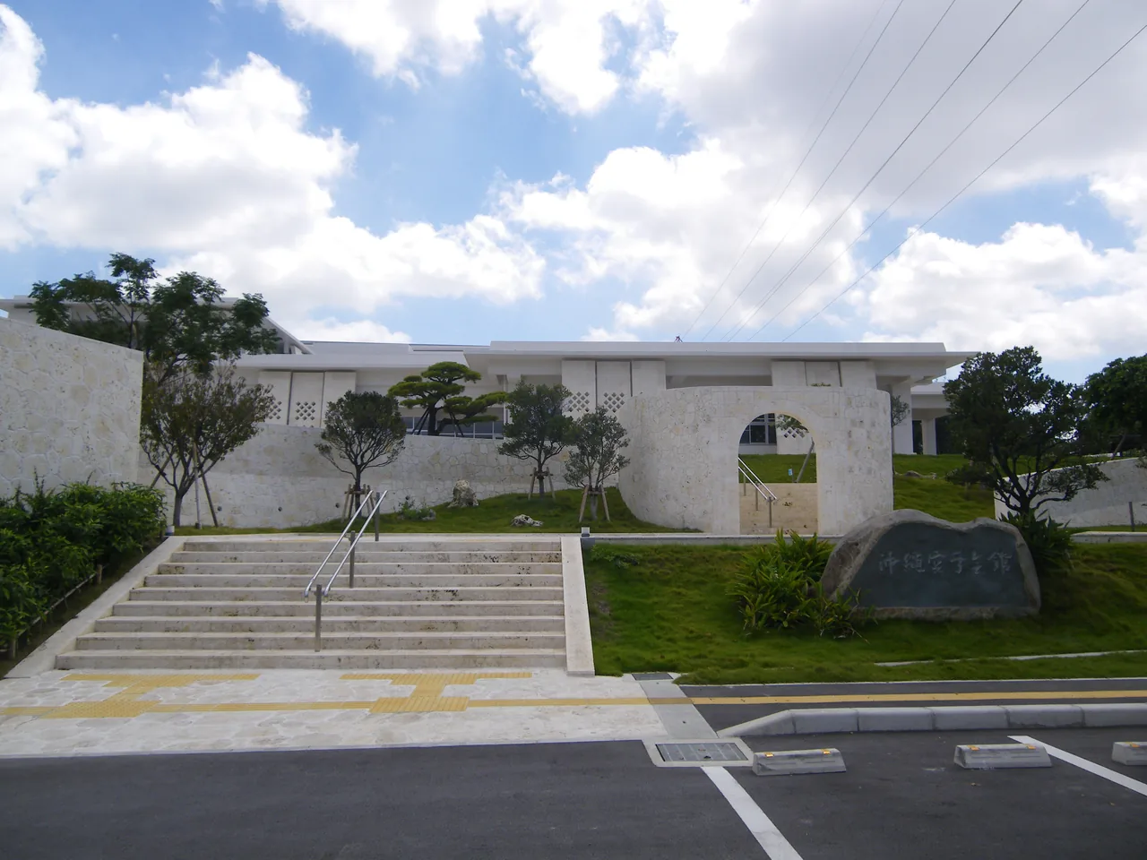 A low white building with a wide flight of steps leading up to it, seen from the car park
