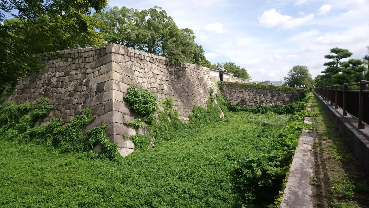 A dry section of castle moat with grass on the bottom and stone walls on both sides