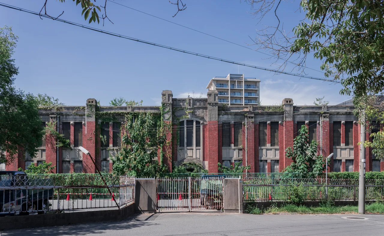 A long red brick building of two storeys behind a metal fence