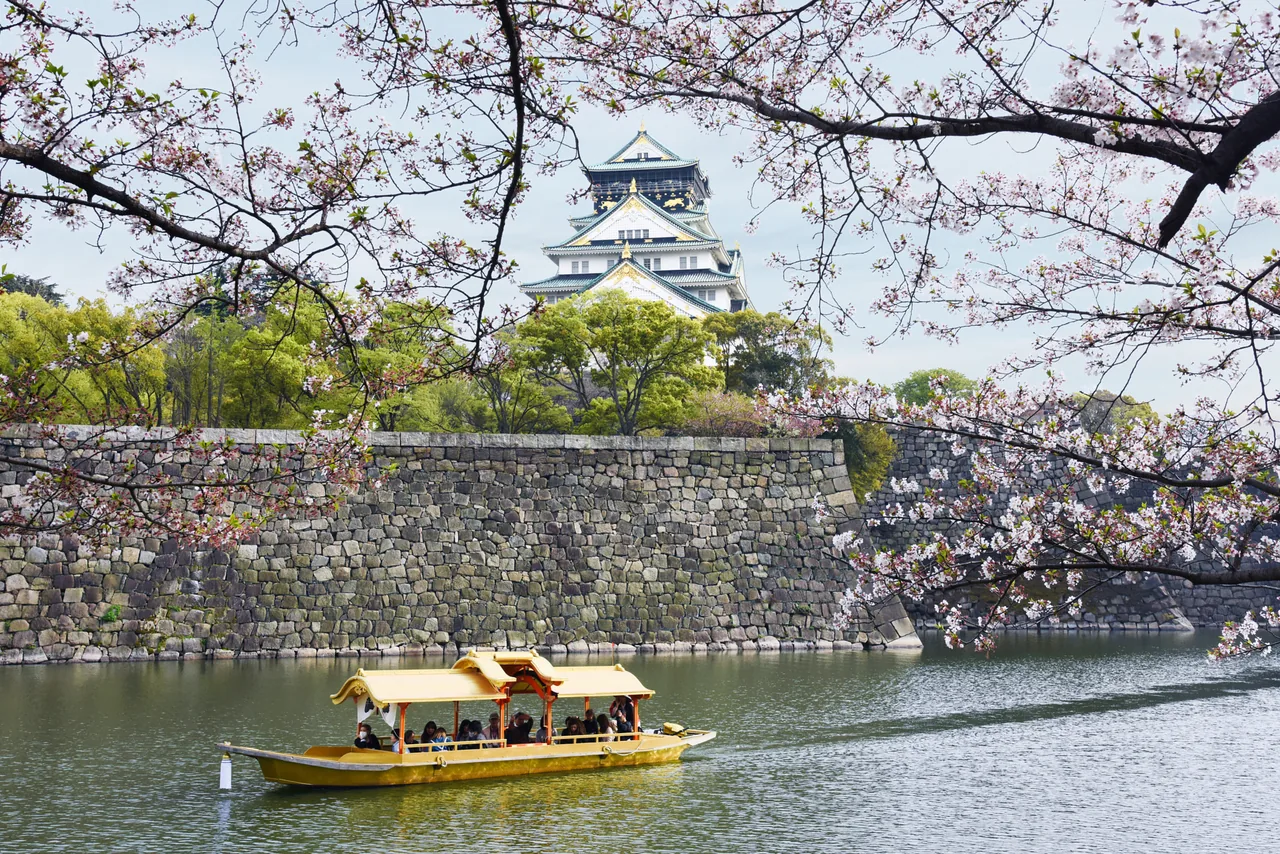 A gold covered boat on the castle moat with blossom and the keep behind it