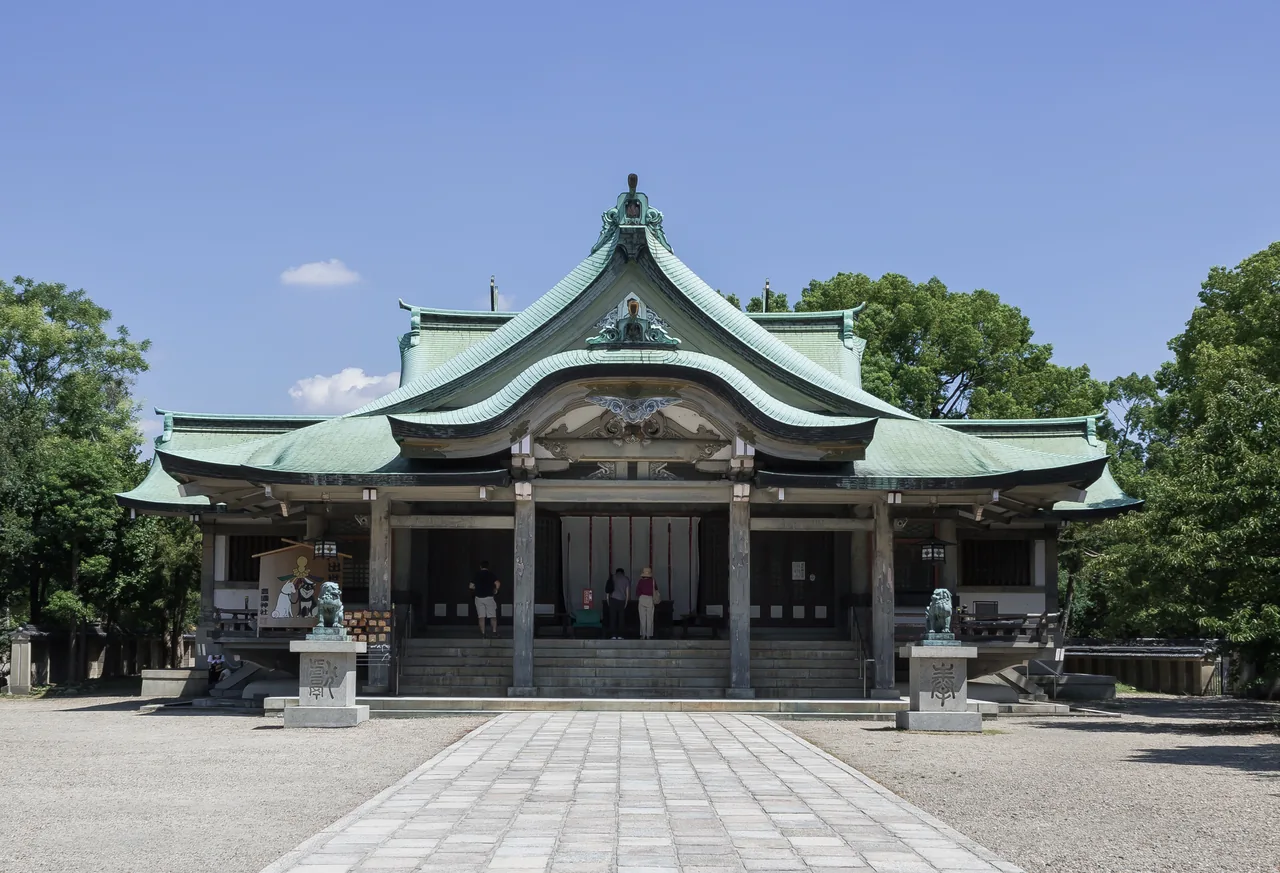 A shrine hall with a green copper roof and stone lions in front of it