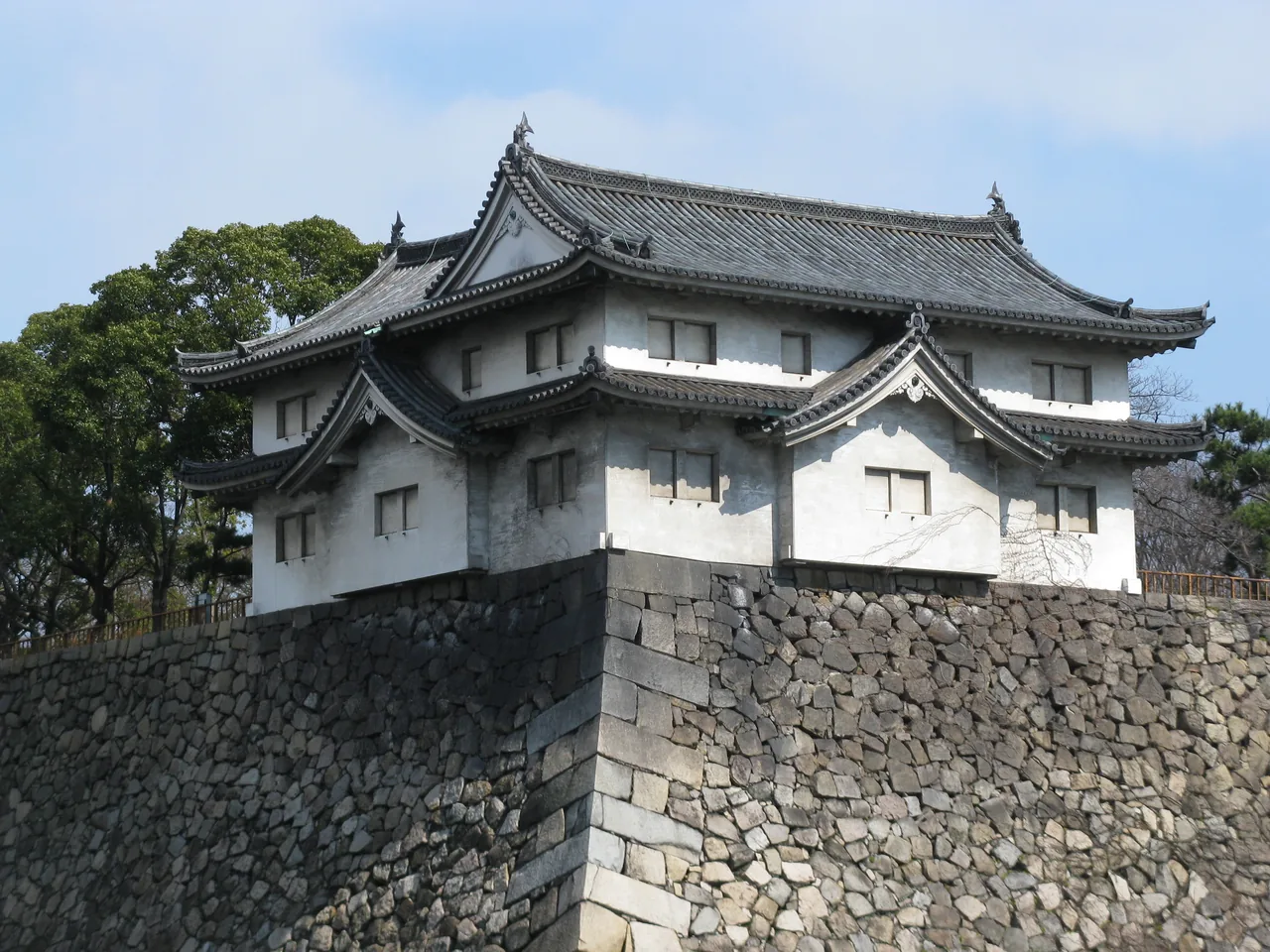 A two storey white turret with black roof tiles standing on a stone base