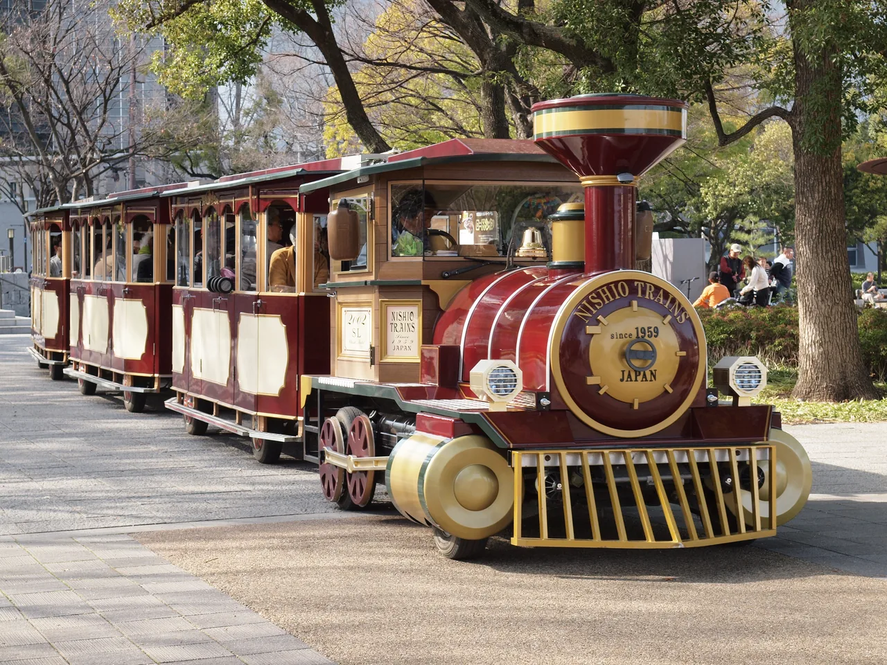 A small road train with open carriages parked on a path in the park