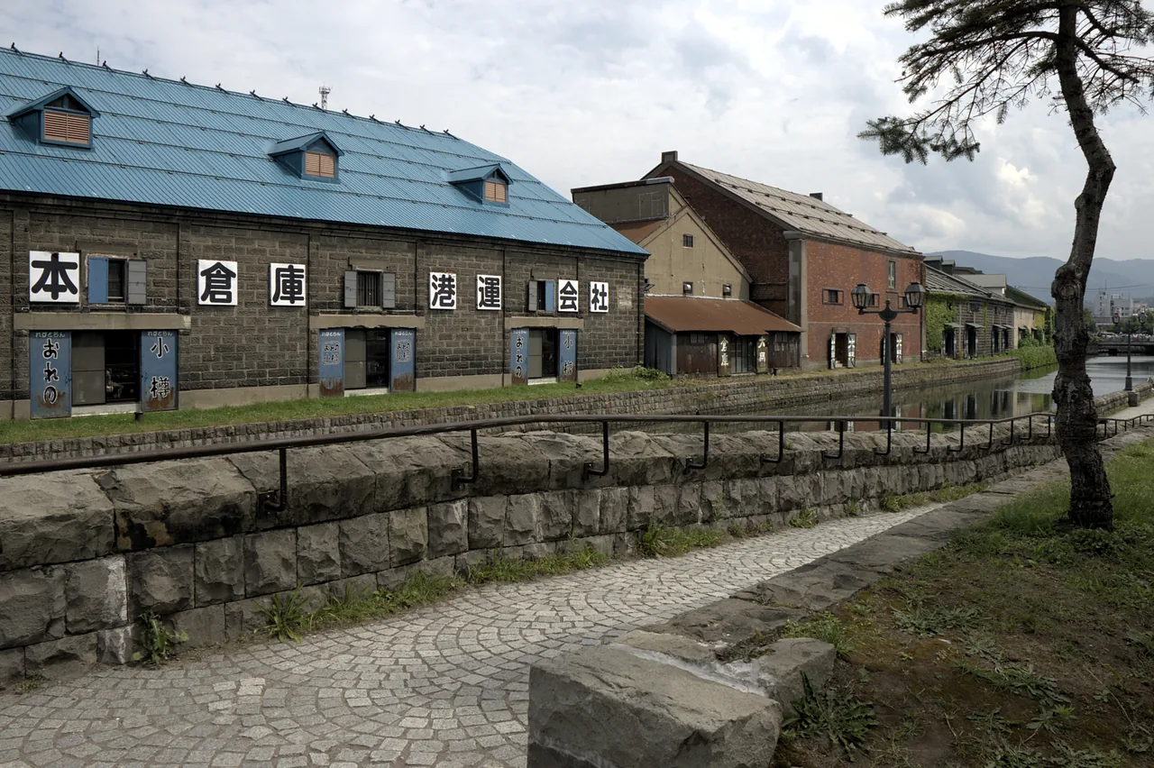 Stone warehouses with blue roofs beside Otaru Canal and a stone walkway on a sunny day