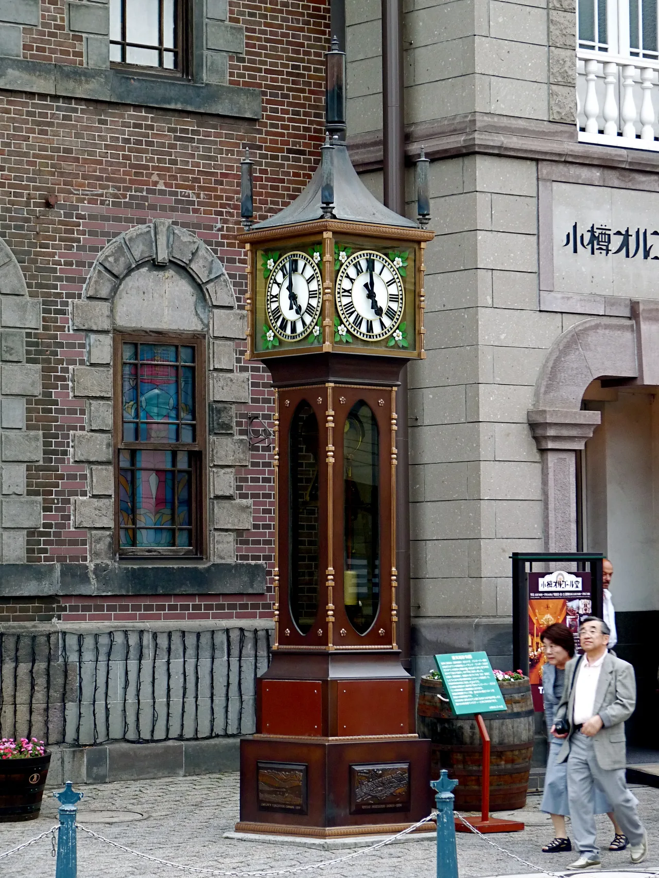Tall steam clock in front of a red-brick building, far taller than the person beside it