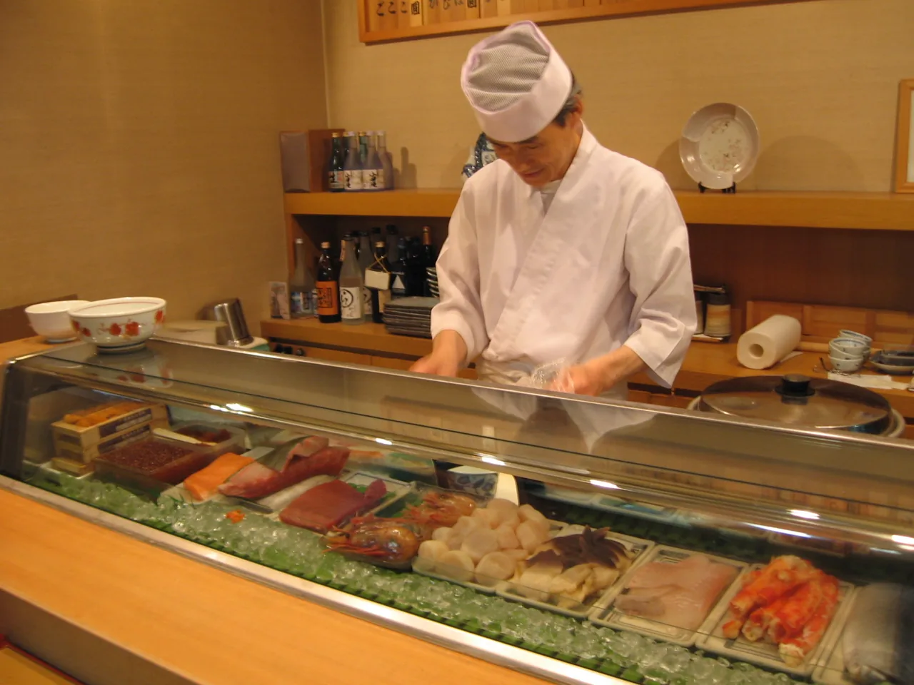 Sushi chef working behind the counter with fish in a glass case