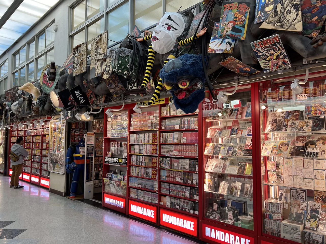 The inside of a Mandarake shop with several Mandarake signs above glass cases of goods
