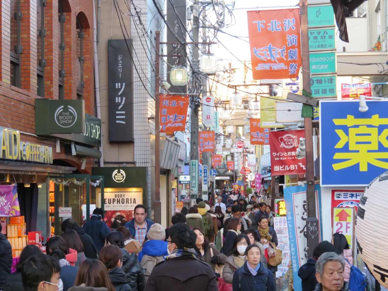 A crowded shopping lane in Shimokitazawa in Tokyo lined with signs and small shopfronts