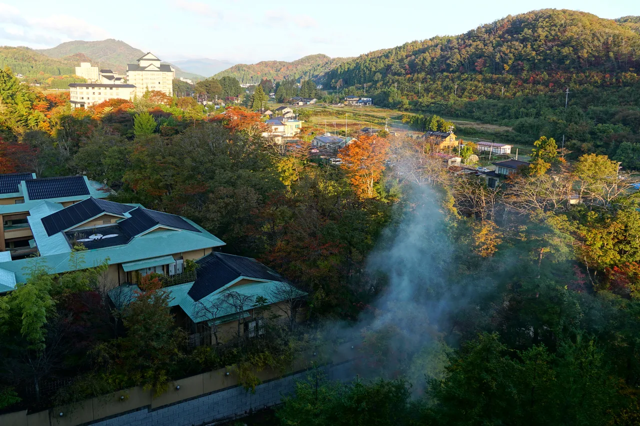 Akiu Onsen seen from above in autumn, inn roofs among coloured hillsides with steam rising from the valley