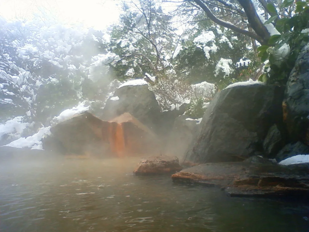 An outdoor hot spring bath at Akiu among snow-covered rocks, with steam rising off the water