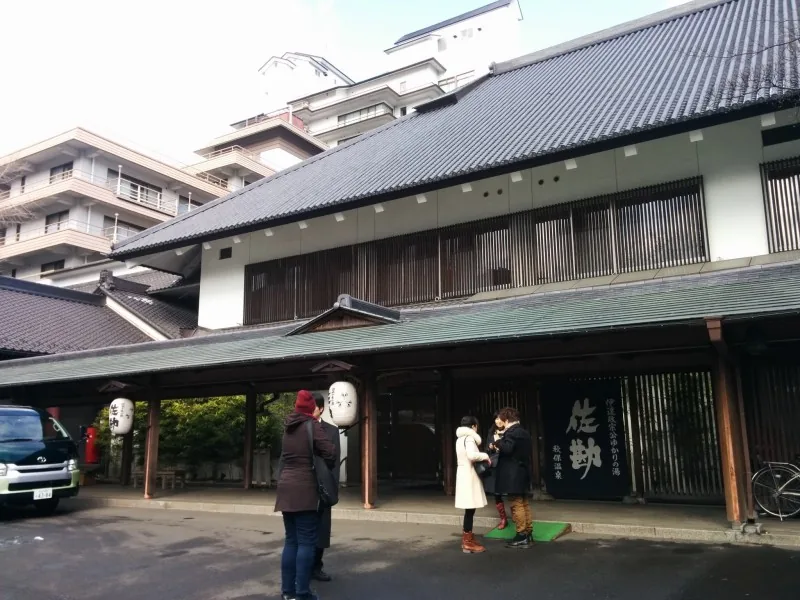 The entrance of Sakan at Akiu Onsen, a tiled roof over a wooden porch with guests standing under it