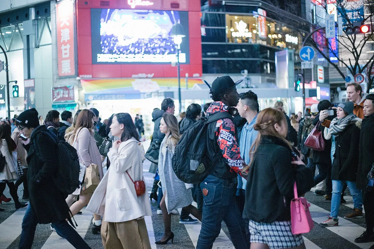 A dense crowd crossing Shibuya Crossing in daylight, shopfronts and screens behind them