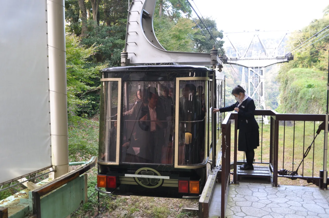 A dark ropeway car at the Nihondaira station with an attendant standing by the door