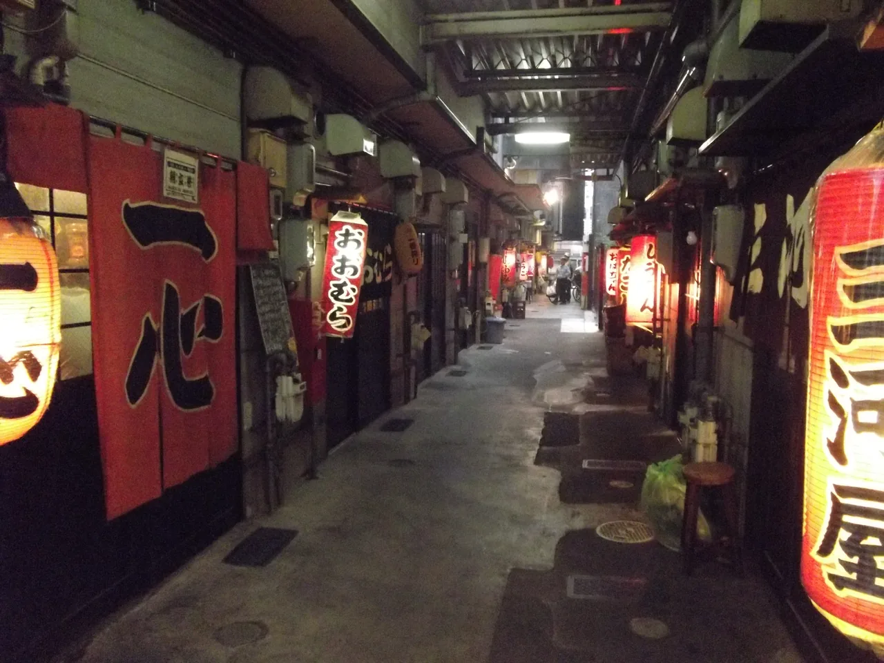 A narrow alley of small oden shops lit by red lanterns
