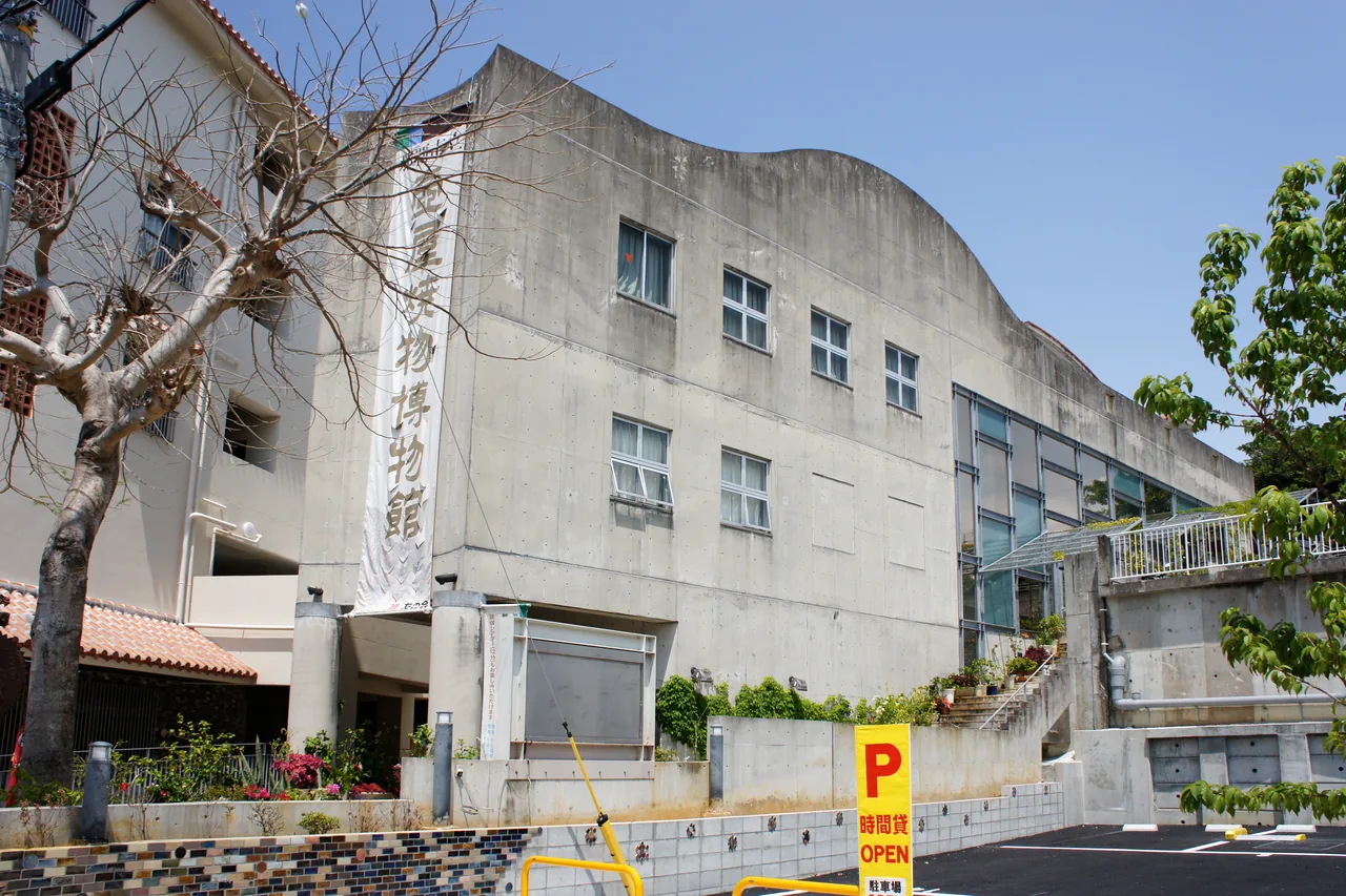 A low building on a sloping street with a vertical museum sign hanging at its corner