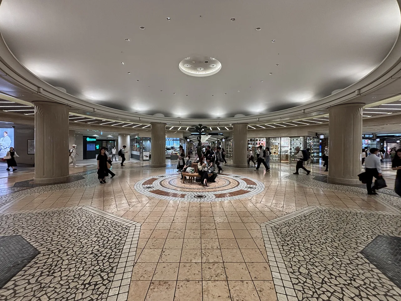 A wide underground shopping concourse with a patterned floor and lit shopfronts