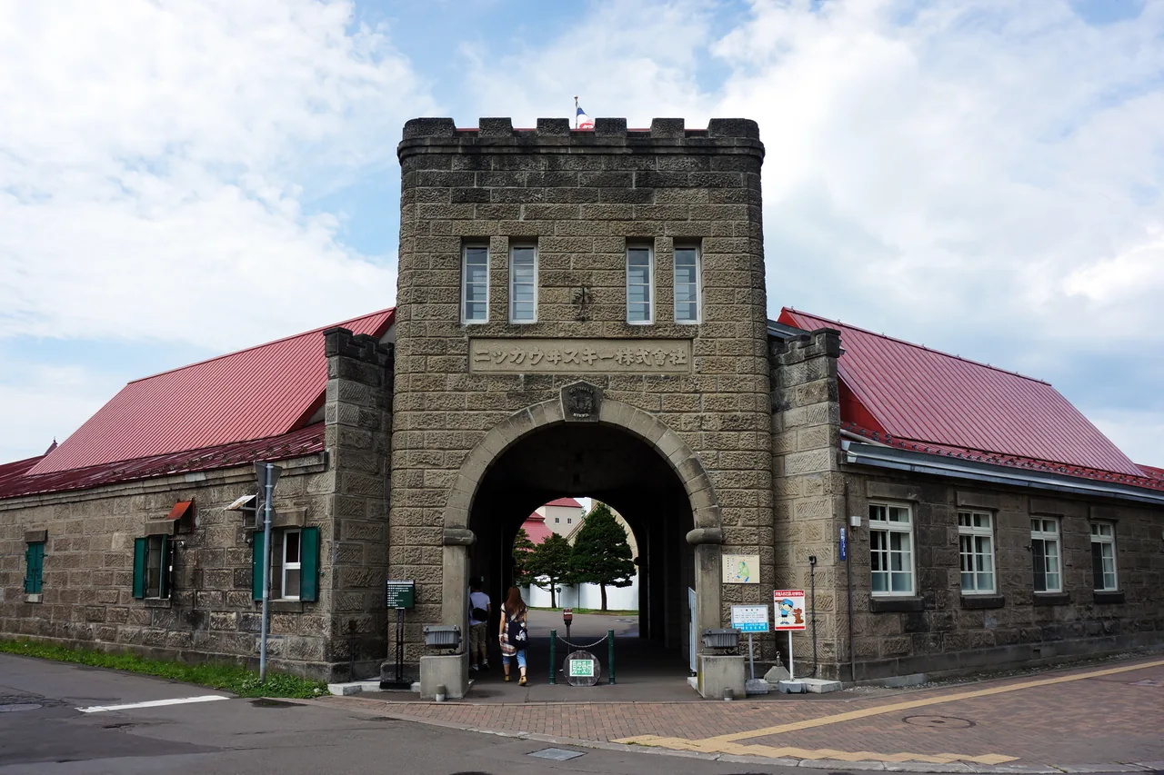Castle-like stone gate between red-roofed stone buildings at a distillery
