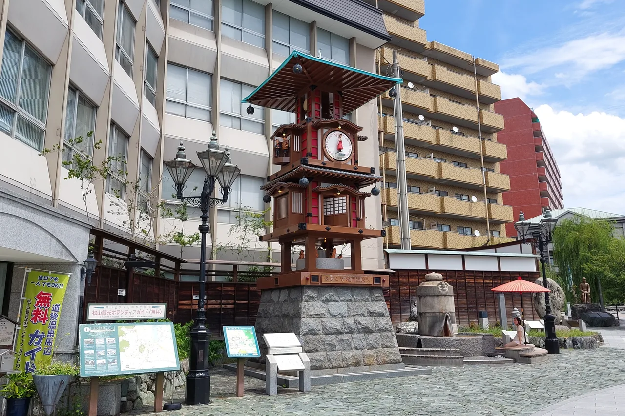 The three-tiered Botchan Karakuri Clock on its stone base in a square, with buildings behind
