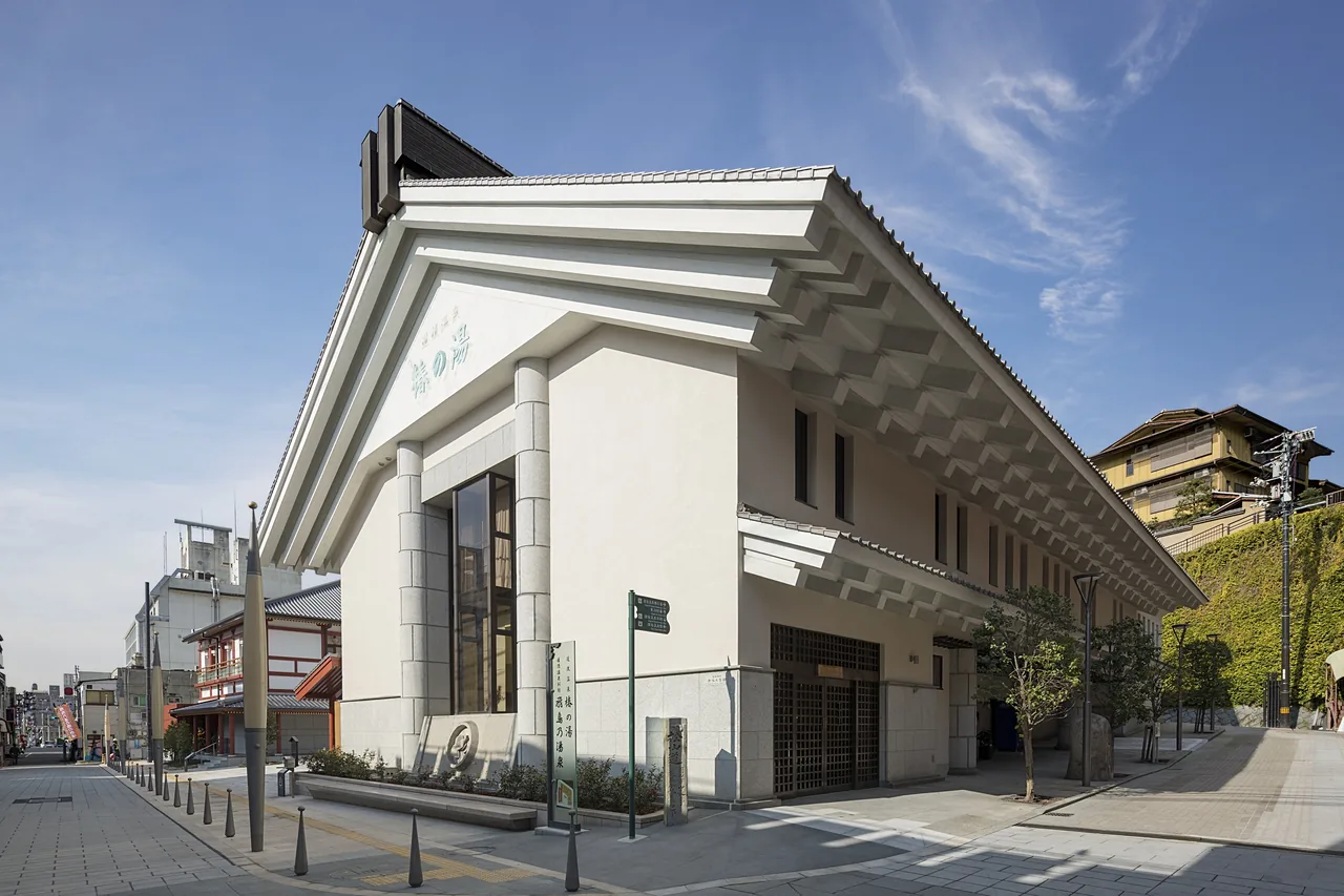 The front of Tsubaki-no-Yu with its white gabled roof under a blue sky, the street empty