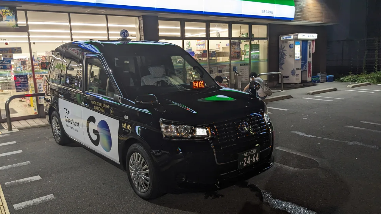 Black JPN TAXI cab parked outside a convenience store at night