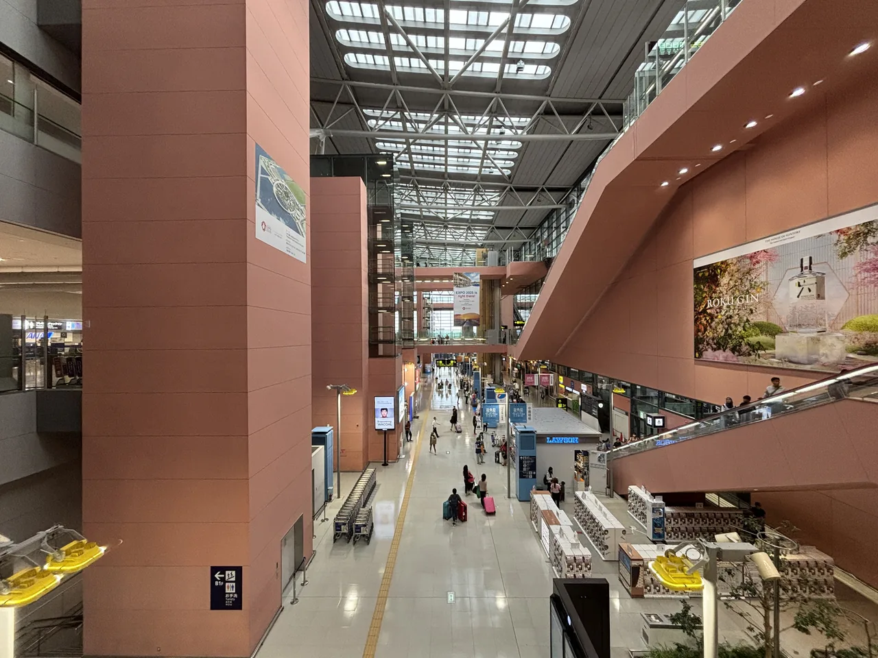Terminal 1 arrival lobby atrium at Kansai Airport with a tall glass roof, brown walls, a few travellers and a Lawson sign